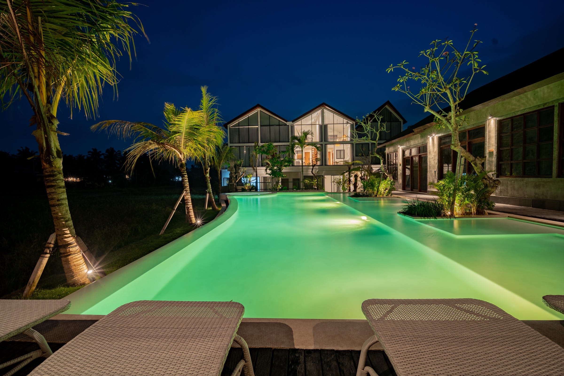The resort pool lit at night, with the two-storey villa glowing behind it