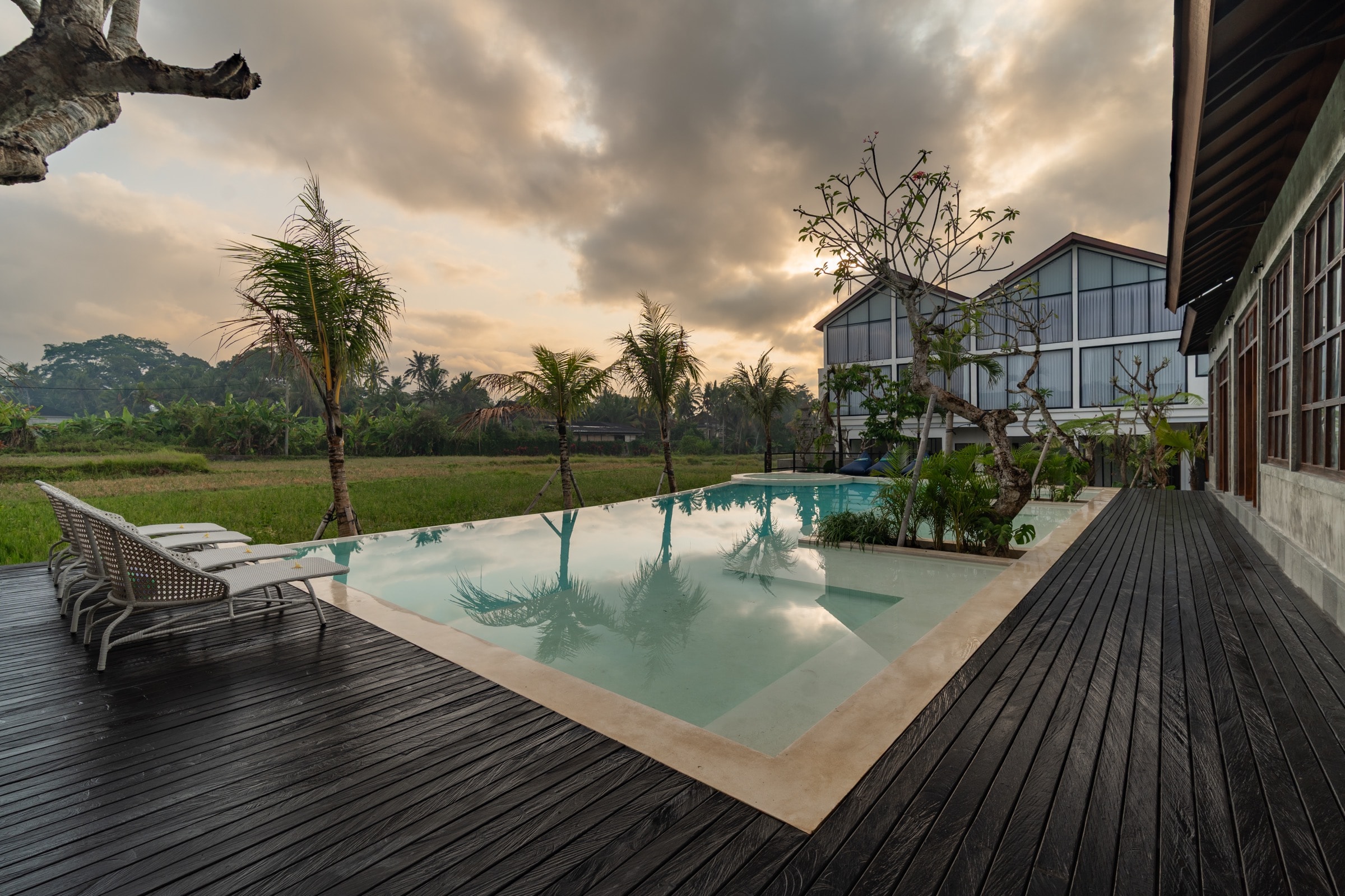 The Santa Ubud Resort at dusk, its two-storey villa lit from within, seen across the pool and rice field