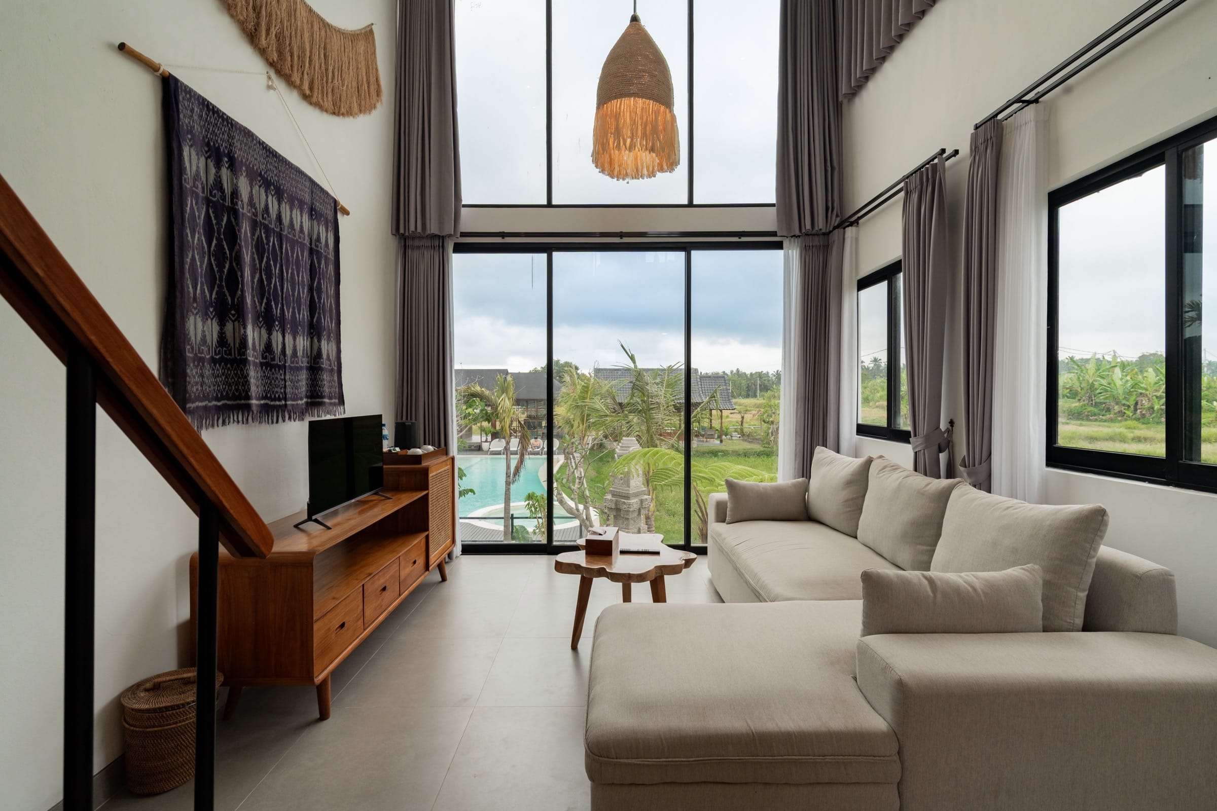 Villa living room with floor-to-ceiling glass opening onto the pool and the rice field beyond